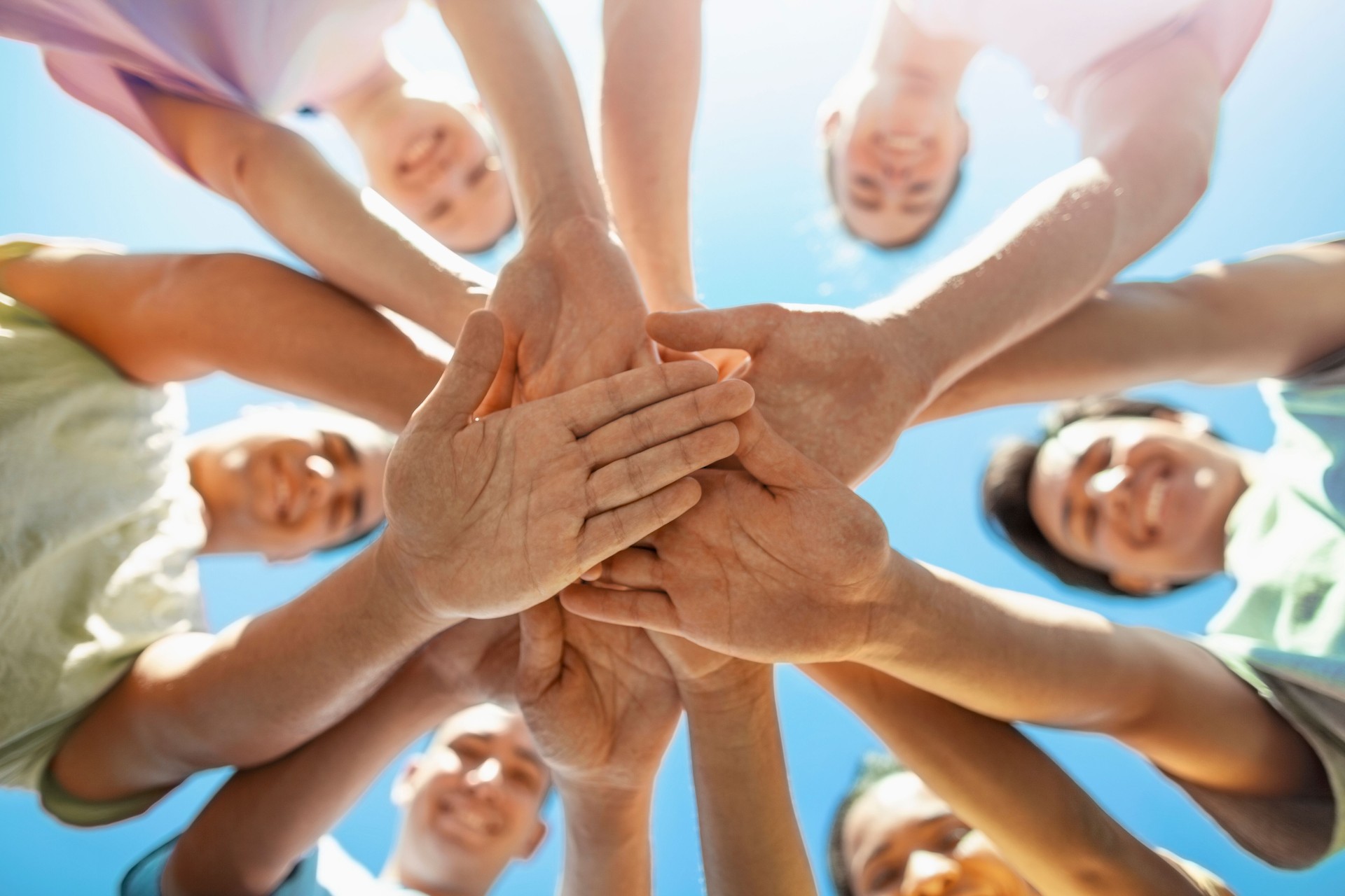 Multiracial group of young men and women students make stacked hands together in community support teamwork success togetherness as environmental social issues volunteers smiling with sky and sunlight